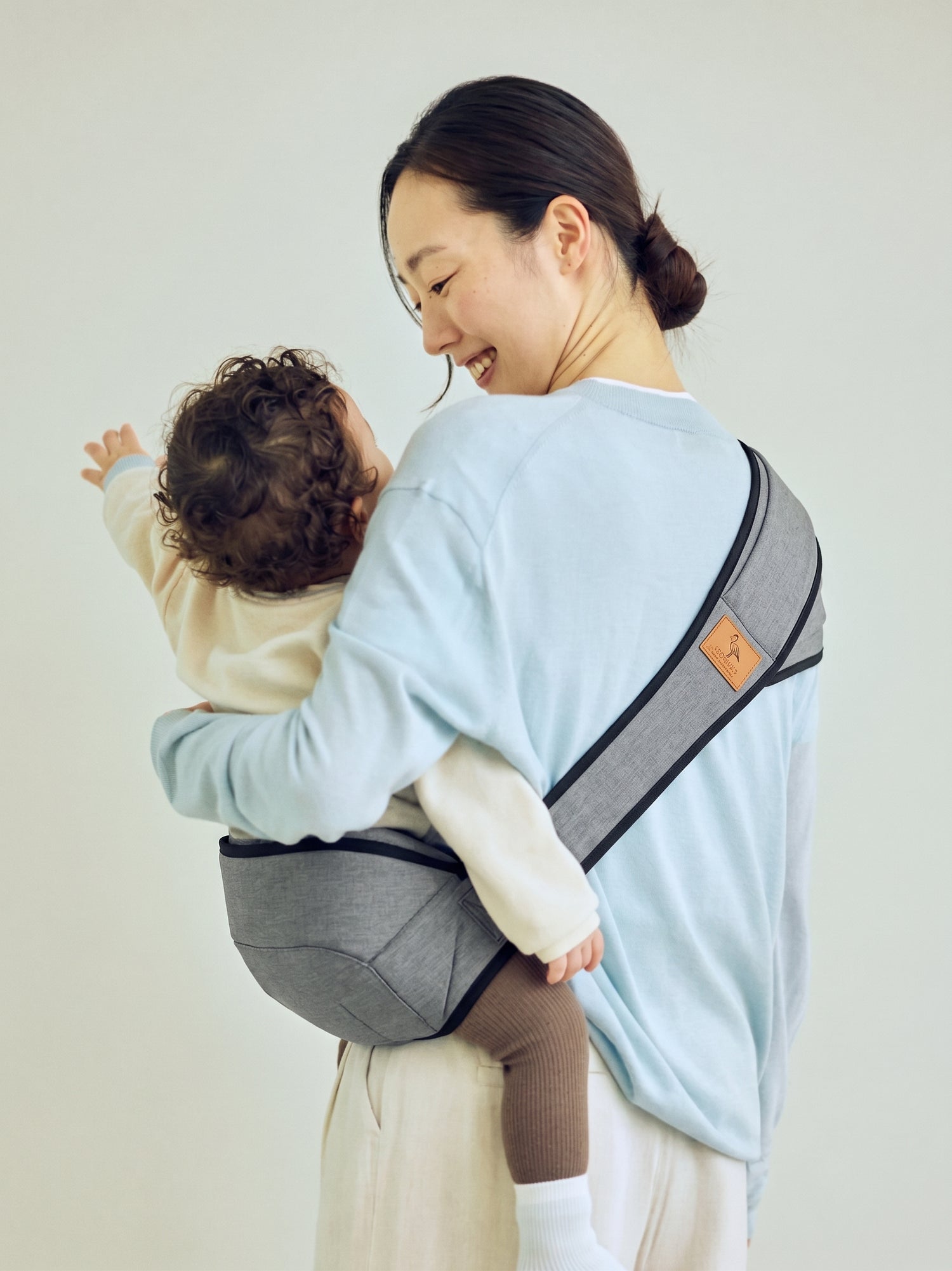 Woman carrying a child in a baby carrier against a plain background